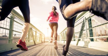 Drei Jogger rennen über eine Brücke.