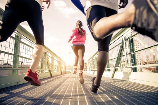 Drei Jogger rennen über eine Brücke.