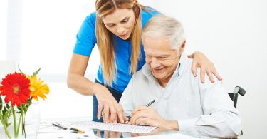 Pflegerin hilft Senior bei einem Kreuzworträtsel