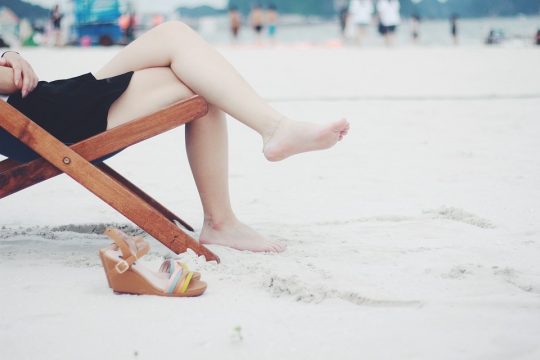 Eine Frau sitzt barfuß in einem Klappstuhl am Strand