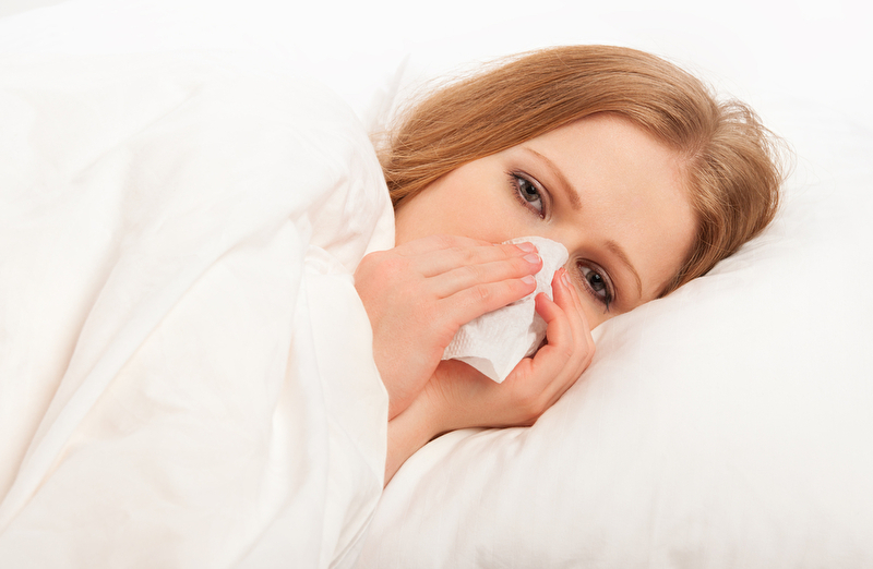 Krankes Mädchen niest im Bett in ein Taschentuch