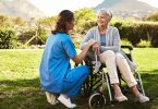 Krankenschwester mit einer älteren Patientin im Rollstuhl.