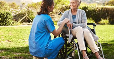 Krankenschwester mit einer älteren Patientin im Rollstuhl.