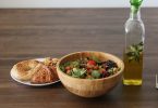 Schüssel mit Gemüsesalat, Gebäck und eine Flasche Olivenöl auf einem Holztisch