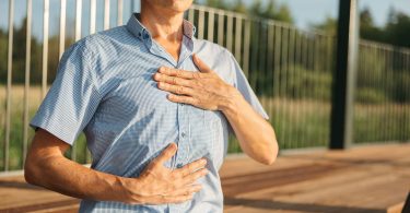 Mann steht auf einer Terrasse und legt eine Hand auf die Brust, die andere auf den Bauch