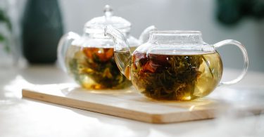 Zwei Glaskannen mit aufgebrühtem Kräutertee auf einem Holzbrett