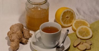 Tasse Tee mit Ingwerwurzel, Zitronenscheiben und einem Glas Honig