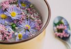 Schale mit Wasser und lila und rosa Blüten, daneben ein Löffel mit Blüten