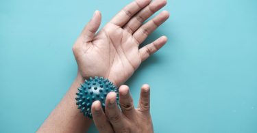 Hände rollen einen Igelball über das Handgelenk vor blauem Hintergrund