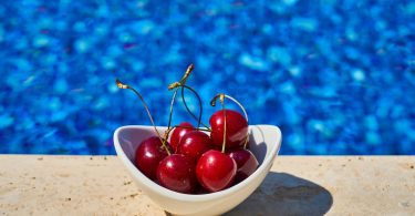 Schale mit frischen Kirschen vor einem blauen Schwimmbecken