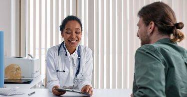 Ärztin im weißen Kittel spricht am Schreibtisch mit einem Patienten