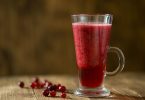 Glas mit rotem Cranberry-Getränk und frischen Cranberrys auf einem Holztisch
