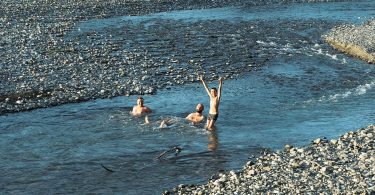 Drei Männer baden in einem kühlen, klaren Fluss mit Kiesufer