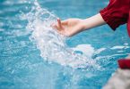 Hand spritzt Wasser in einem blauen Becken auf