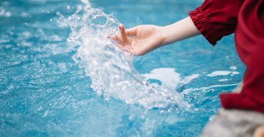 Hand spritzt Wasser in einem blauen Becken auf