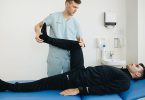 Physiotherapeut dehnt das gestreckte Bein eines Mannes, der auf einer Behandlungsliege liegt