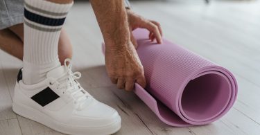 Person in Turnschuhen rollt eine rosa Gymnastikmatte auf einem Holzboden