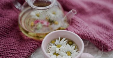 Glaskanne und Tasse mit Blütentee auf einer gestrickten Decke