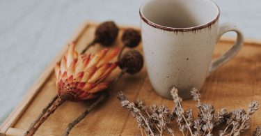 Keramikbecher auf einem Holztablett mit getrockneten Blumen und Lavendel