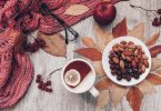 Tasse Tee mit Zitrone, Mandeln, Herbstlaub und ein Strickschal, von oben gesehen