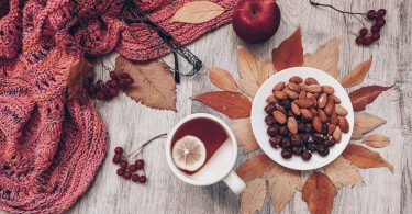 Tasse Tee mit Zitrone, Mandeln, Herbstlaub und ein Strickschal, von oben gesehen