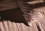 Zerwühltes Bett mit Kissen und Laken im weichen Licht