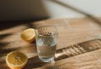Glas Wasser und halbierte Zitronen auf einem Holztisch im Sonnenlicht