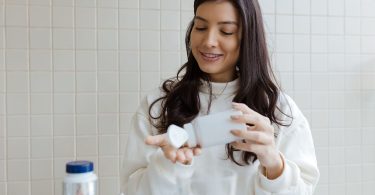 Junge Frau schüttet Kapseln eines Nahrungsergänzungsmittels aus einer Dose in ihre Hand