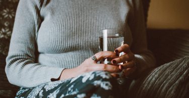 Hände halten ein Glas Wasser vor einem grauen Pullover