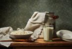 Schale mit Hüttenkäse und ein Glas Milch auf einem Holztisch