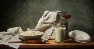 Schale mit Hüttenkäse und ein Glas Milch auf einem Holztisch