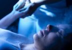 Frau liegt entspannt mit geschlossenen Augen im blauen Licht, die Hände über dem Kopf