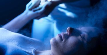 Frau liegt entspannt mit geschlossenen Augen im blauen Licht, die Hände über dem Kopf