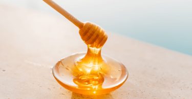 Honig fließt von einem Honiglöffel auf einen kleinen Glasteller