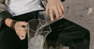 Person gießt Wasser aus einem Glas in eine Karaffe