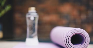 Zusammengerollte violette Gymnastikmatte und eine Wasserflasche