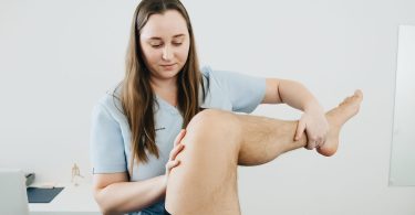Physiotherapeutin bewegt das angewinkelte Bein eines Patienten im Knie