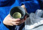 Hände halten einen Becher mit heißem Zitronenwasser, daneben Taschentücher