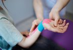 Therapeutin legt ein blaues und rosa Kinesio-Tape an einem Handgelenk an