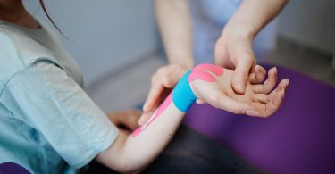 Therapeutin legt ein blaues und rosa Kinesio-Tape an einem Handgelenk an