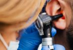 Ärztin mit Handschuhen untersucht mit einem Otoskop das Ohr eines Mannes