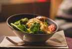 Schüssel mit grünem Salat und gegrilltem Hähnchen auf einem Holzbrett
