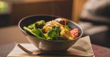 Schüssel mit grünem Salat und gegrilltem Hähnchen auf einem Holzbrett
