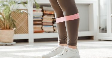 Beine mit einem rosa Gymnastikband über den Knien in einem hellen Wohnraum