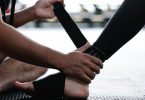 Hände legen eine schwarze Bandage an einem Fußgelenk an