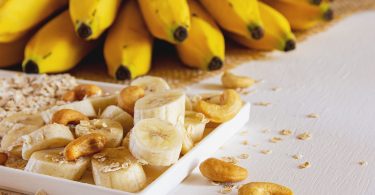 Bananenscheiben, Cashewkerne und Haferflocken, dahinter Bananen